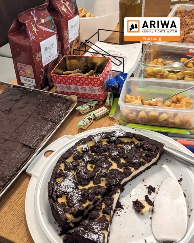 Tisch mit veganen Weihnachtsleckereien bei der ARIWA-Jahresabschlussfeier 2025: angeschnittene Schokoladentarte, Brownies, Spekulatius, karamellisierte Nüsse und Süßigkeiten. Oben rechts das ARIWA-Logo Würzburg.