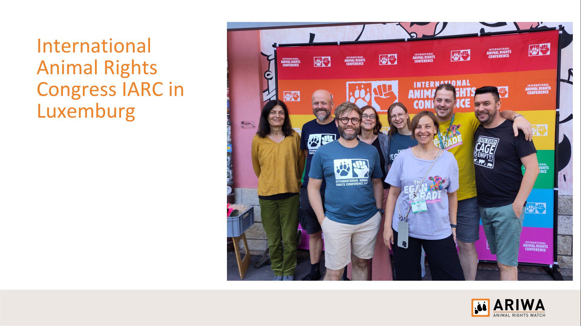 Präsentationsfolie „International Animal Rights Congress IARC in Luxemburg": Gruppenfoto von etwa acht Personen vor dem bunten Regenbogen-Rollup der Konferenz. Teilnehmende tragen IARC- und „The Vegan Parade"-T-Shirts.